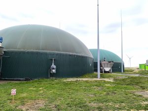 Zbiorniki instalacji biogazowej z zielonymi kopułami, z turbiną wiatrową w tle.